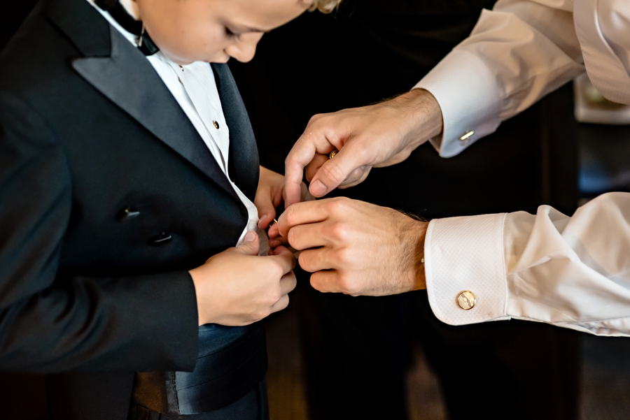 A groom helps his ring bearer with his suit.